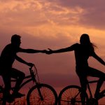 A photo of two people on bicycles against a cloudy sunset sky