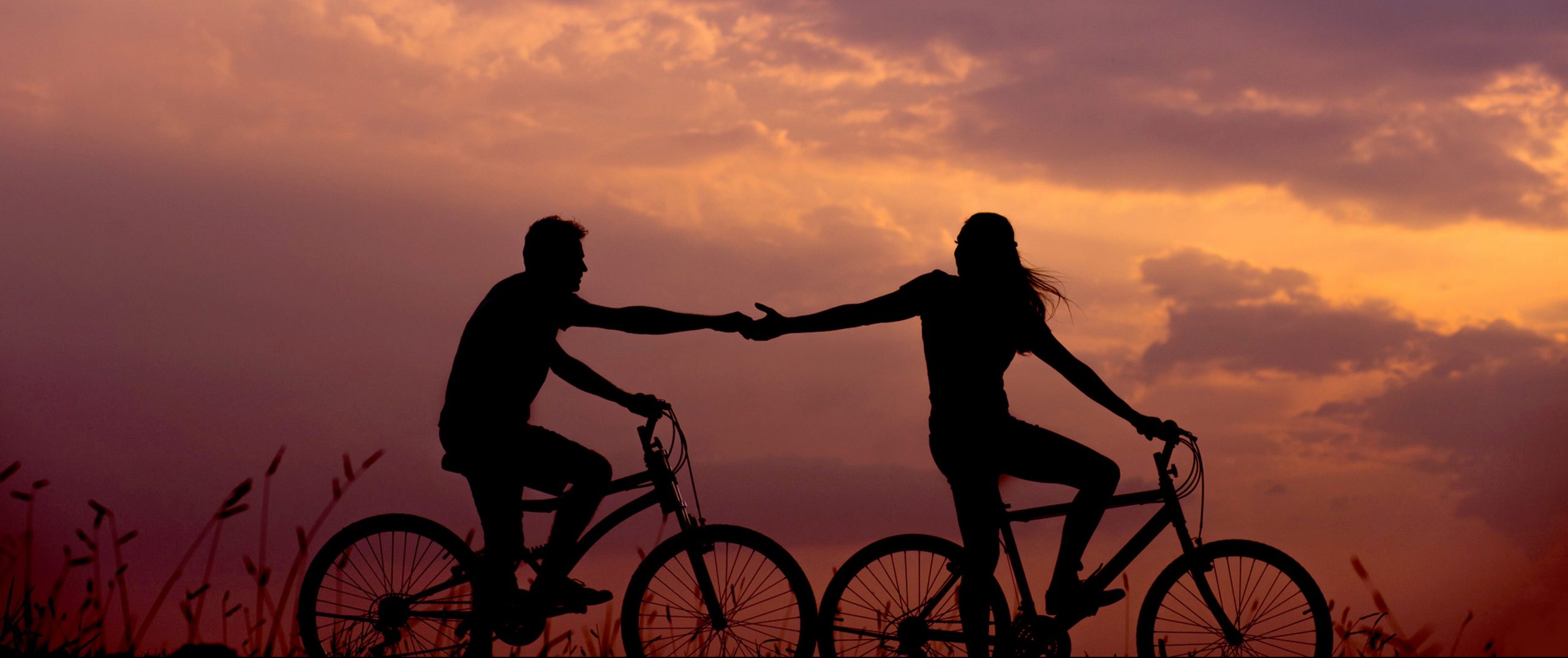A photo of two people on bicycles against a cloudy sunset sky